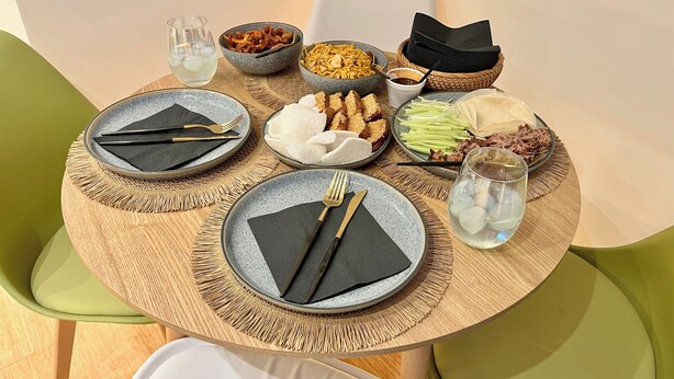 Una mesa redonda de comedor con platos, cubiertos y diferentes platos, rodeada de sillas verdes.