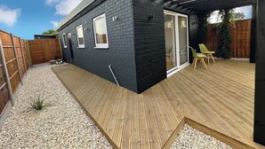 Una casa moderna con fachada negra, una terraza de madera y un ventanal corredero que da a una zona de estar al aire libre.