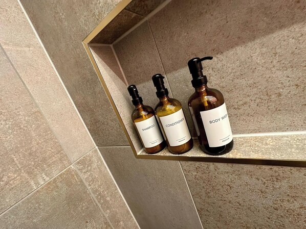Three bottles of body wash, conditioner, and shampoo on a shelf against a tiled wall. - Luxurious Guest House in Yorkshire With Parking (Selby)