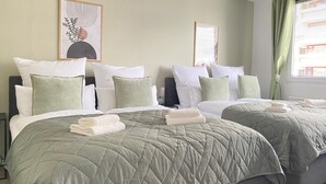 A hotel room with two beds, each with green bedding and white pillows, a large window with curtains, and artwork on the walls.
