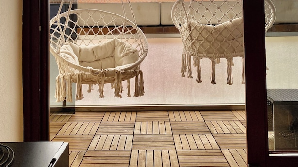 A room with a view of the sea, featuring two macramé swing chairs and a wooden floor.