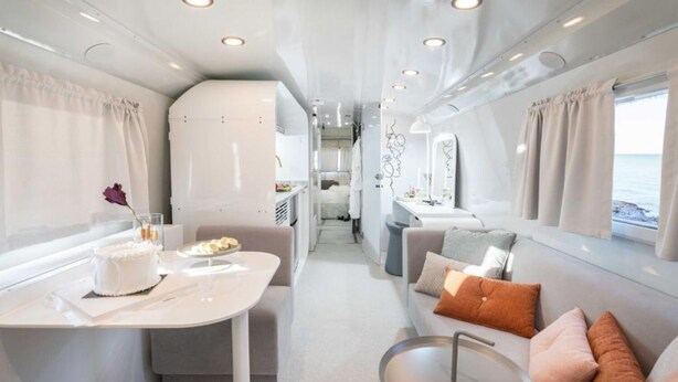 A modern interior with a dining area, a sofa with cushions, and a view of the sea. - The Daydream Bus Hideaway by Sea N' Rent (Gesher HaZiv)
