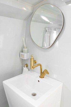 Un baño con un lavamanos blanco, grifo dorado y un espejo redondo.