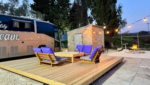 A bus converted into a stationary living space with a deck, seating, and a small stone structure. - The Daydream Bus Hideaway by Sea N' Rent (Gesher HaZiv)