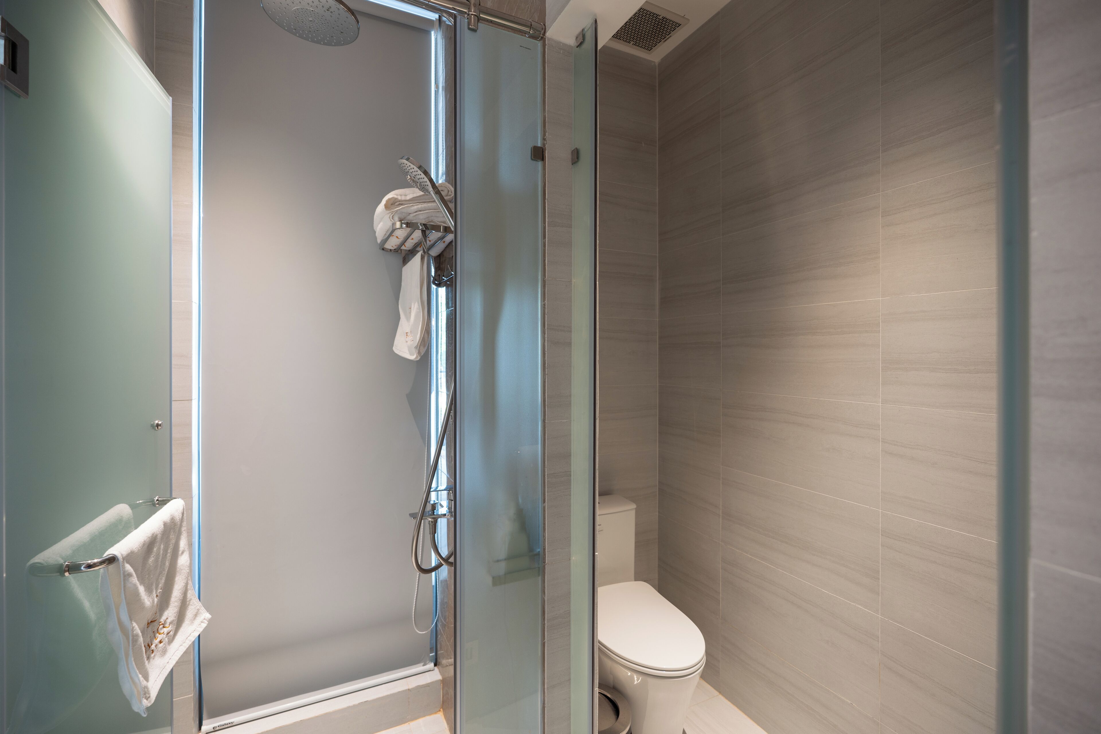A modern bathroom with a glass-enclosed shower, a toilet, and a towel rack.