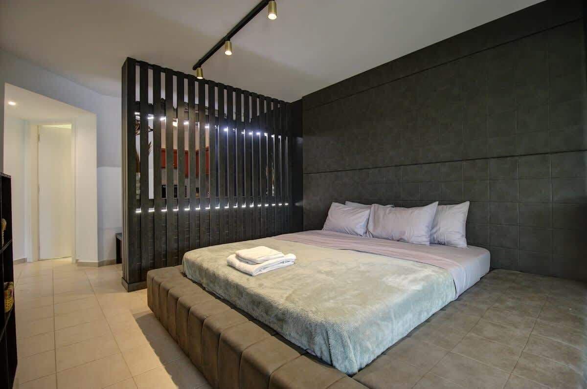 Un dormitorio moderno con una cama grande, un banco al pie de la cama y una pared oscura con listones verticales.