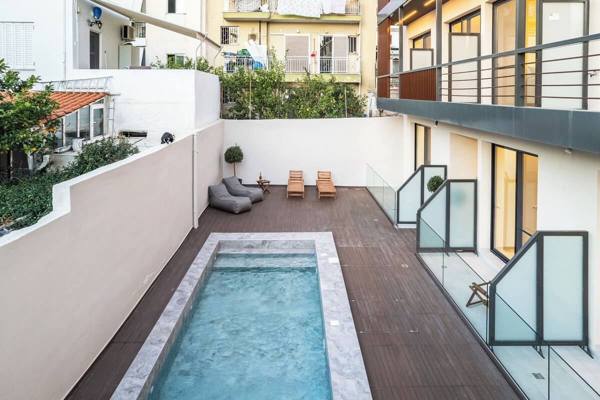 Un área de piscina en la azotea con un pequeño rincón de estar y vistas de los edificios circundantes.