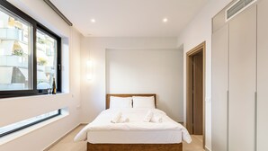 Una habitación de hotel moderna con una cama grande, un ventanal con vistas a edificios y un armario.