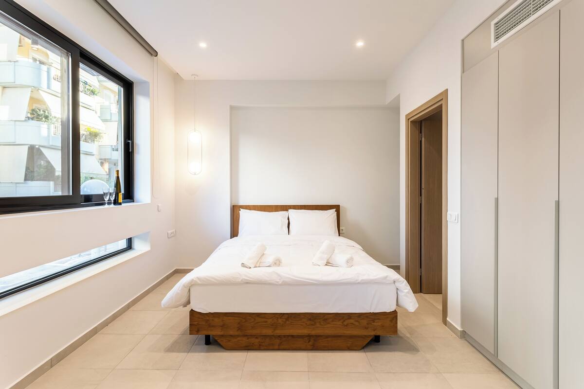 Una habitación de hotel moderna con una cama grande, un ventanal con vistas a edificios y un armario.
