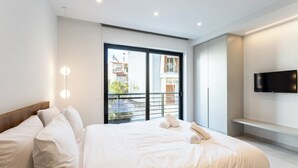 Una habitación de hotel moderna con una cama grande, un televisor montado en la pared y un balcón con vistas a edificios.