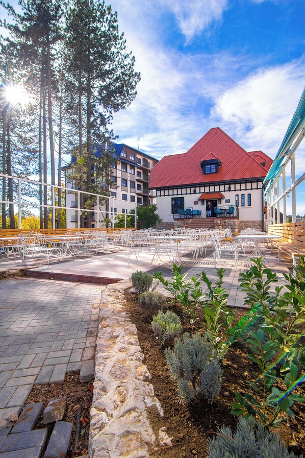 An outdoor seating area with tables and chairs, a stone pathway, and a building with a red roof in the background.