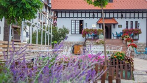 A traditional European building with a red-tiled roof, white walls, and a balcony with blue chairs.