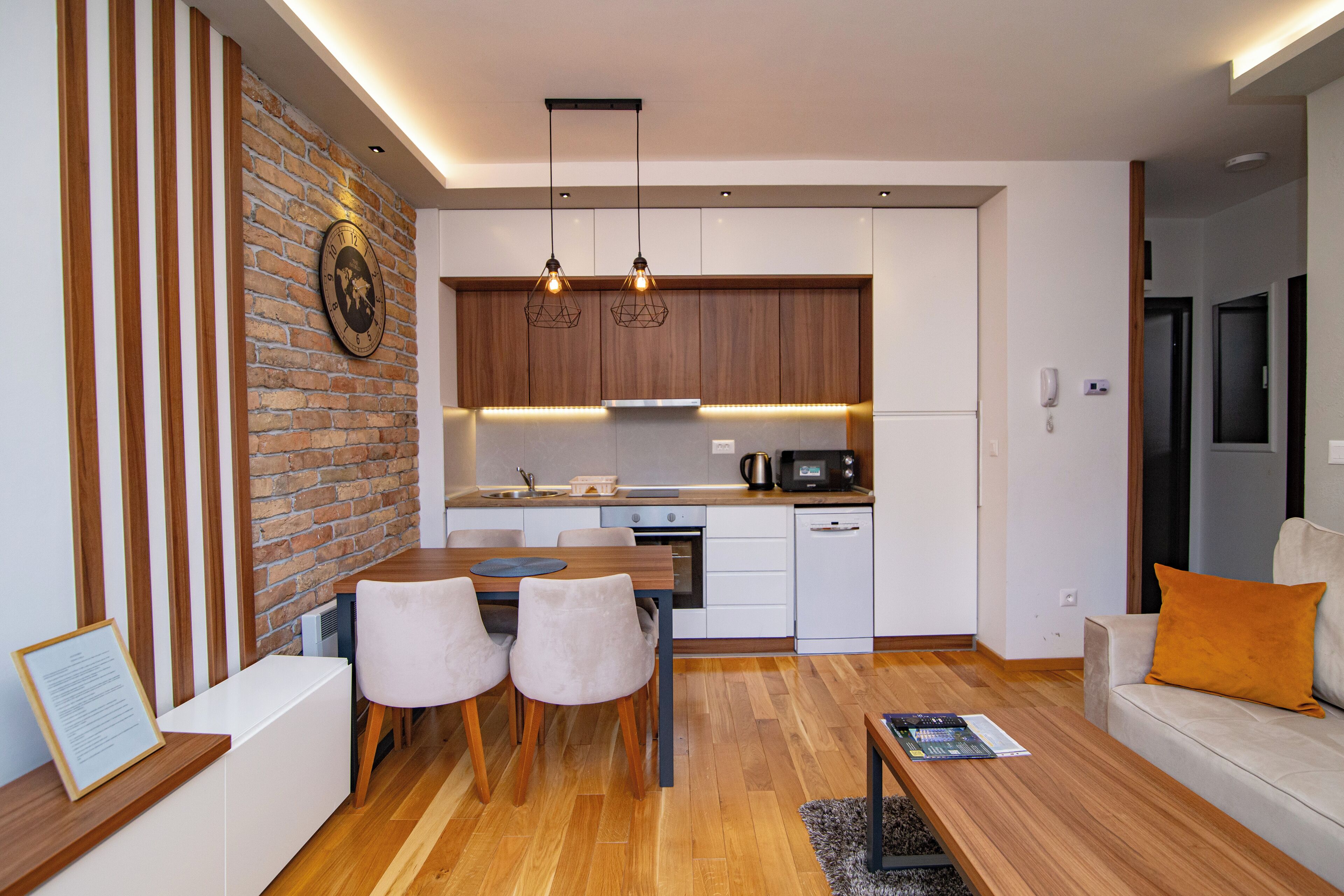 A modern kitchen with wooden cabinets, a brick accent wall, and pendant lighting.