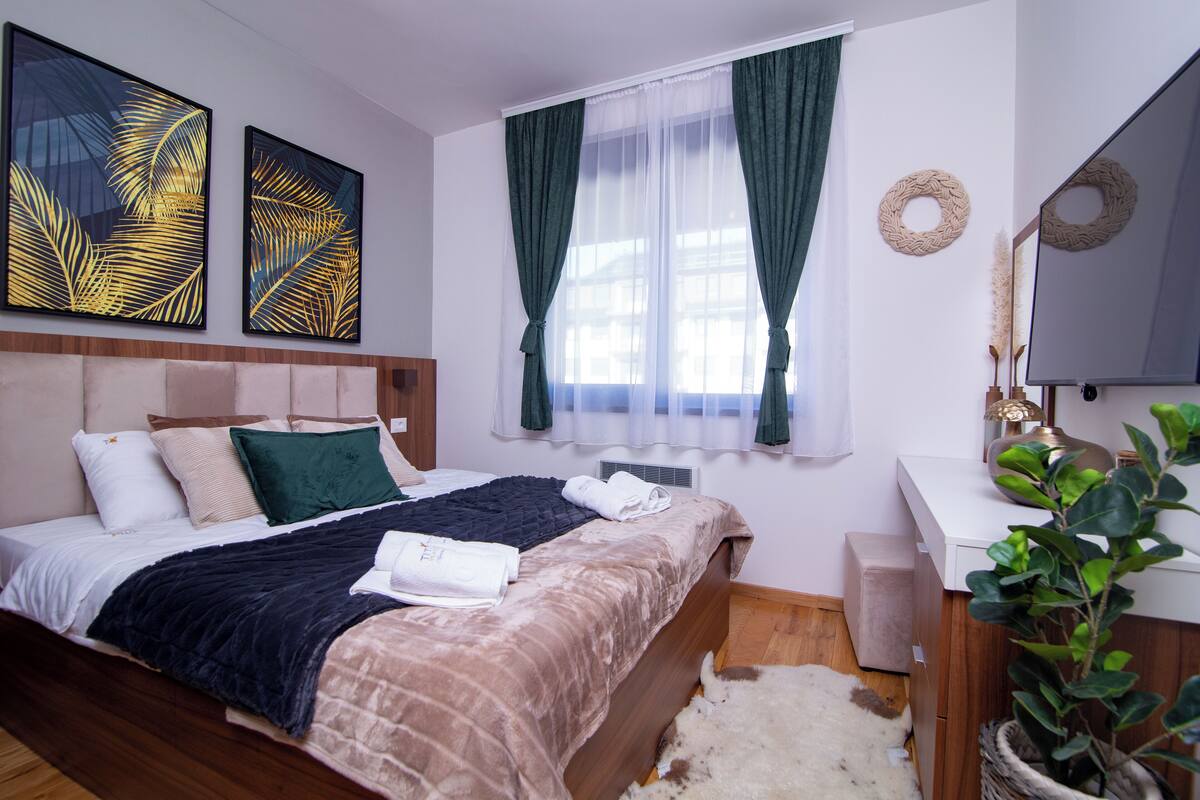 A bedroom with a bed, a bedside table, a mirror, and a window with curtains.