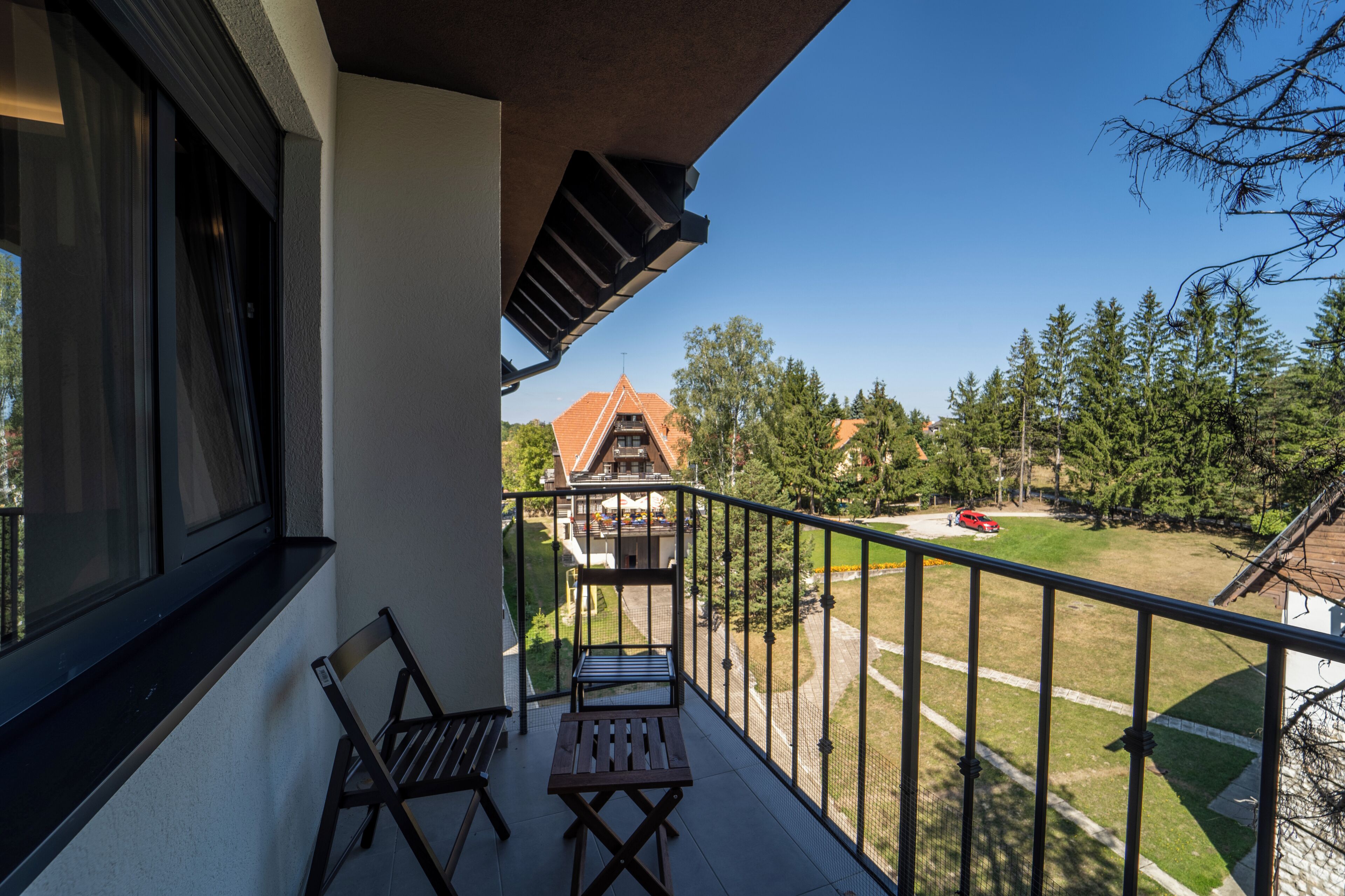 A balcony with a table and two chairs, overlooking a residential area with houses and trees.