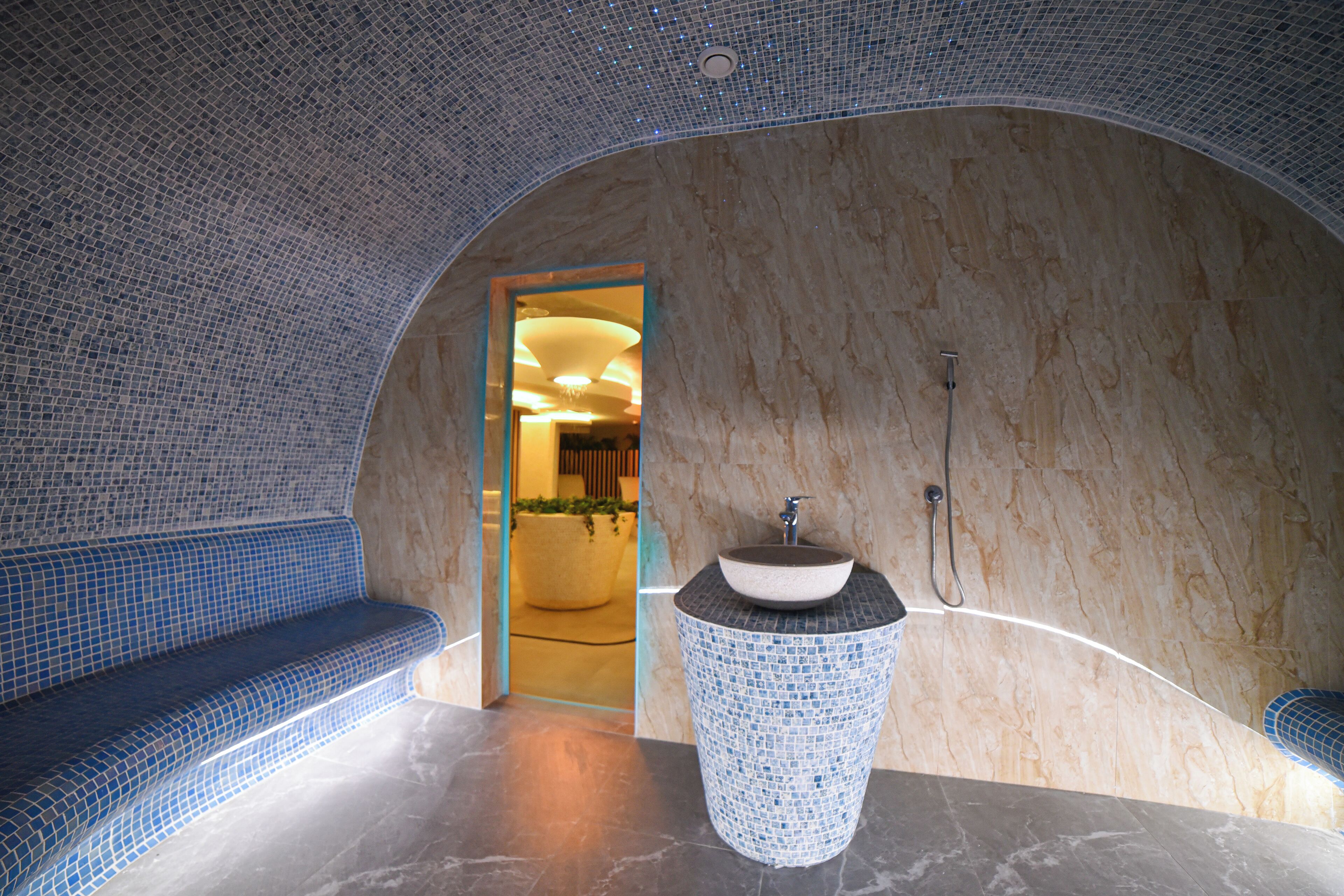 Un baño con un banco de mosaicos, un lavamanos con encimera de mármol y un techo curvo.