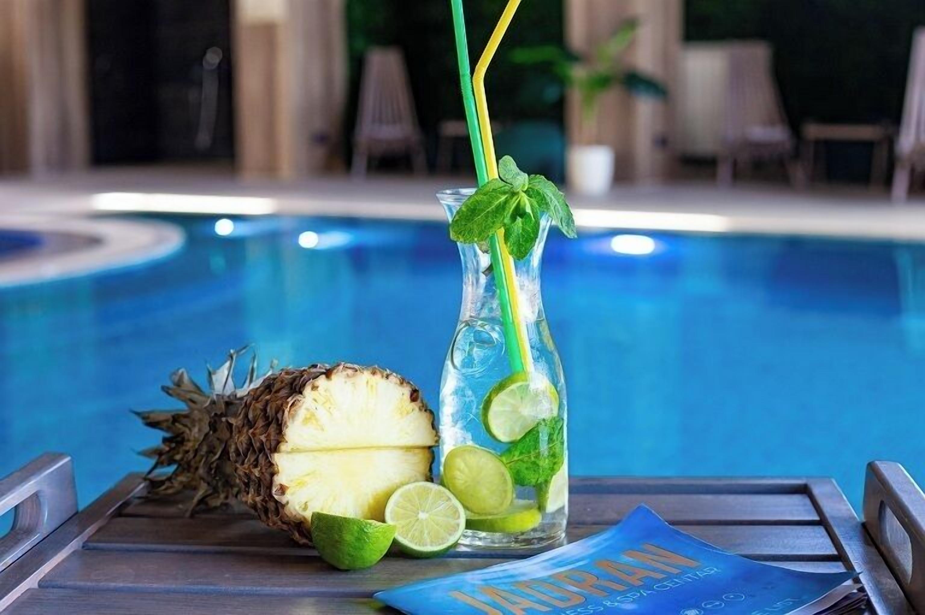 Escena junto a la piscina con una piña, rodajas de limón y una bebida con pajita y adorno de menta.