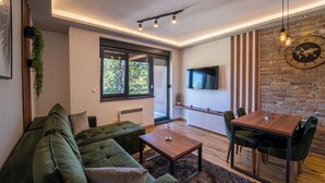 A modern living room with a green sofa, wooden coffee table, and a dining area with a wooden table and chairs.