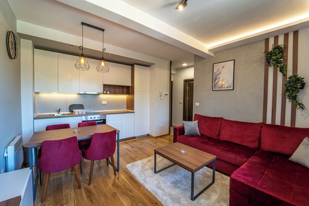 A modern living room with a red sofa, a wooden coffee table, and a dining area with a wooden table and red chairs.