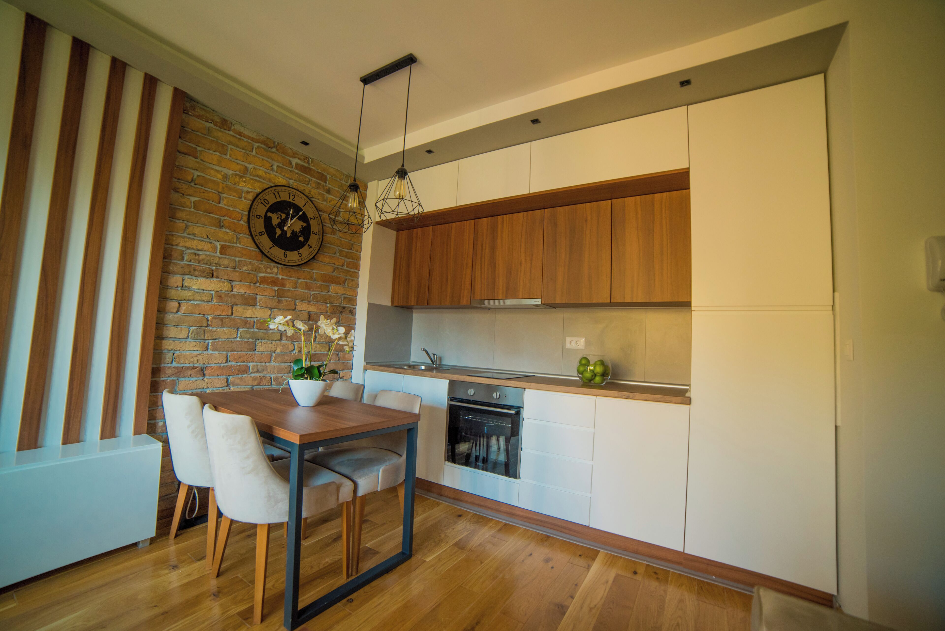 A modern kitchen with wooden cabinets, a brick wall, and a dining area with a table and chairs.