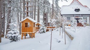 A wooden cabin and a traditional building with a red roof, surrounded by snow-covered trees and a snow-covered path.
