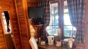 Quarto de cabana de madeira com escrivaninha, cadeira e televisão na parede.