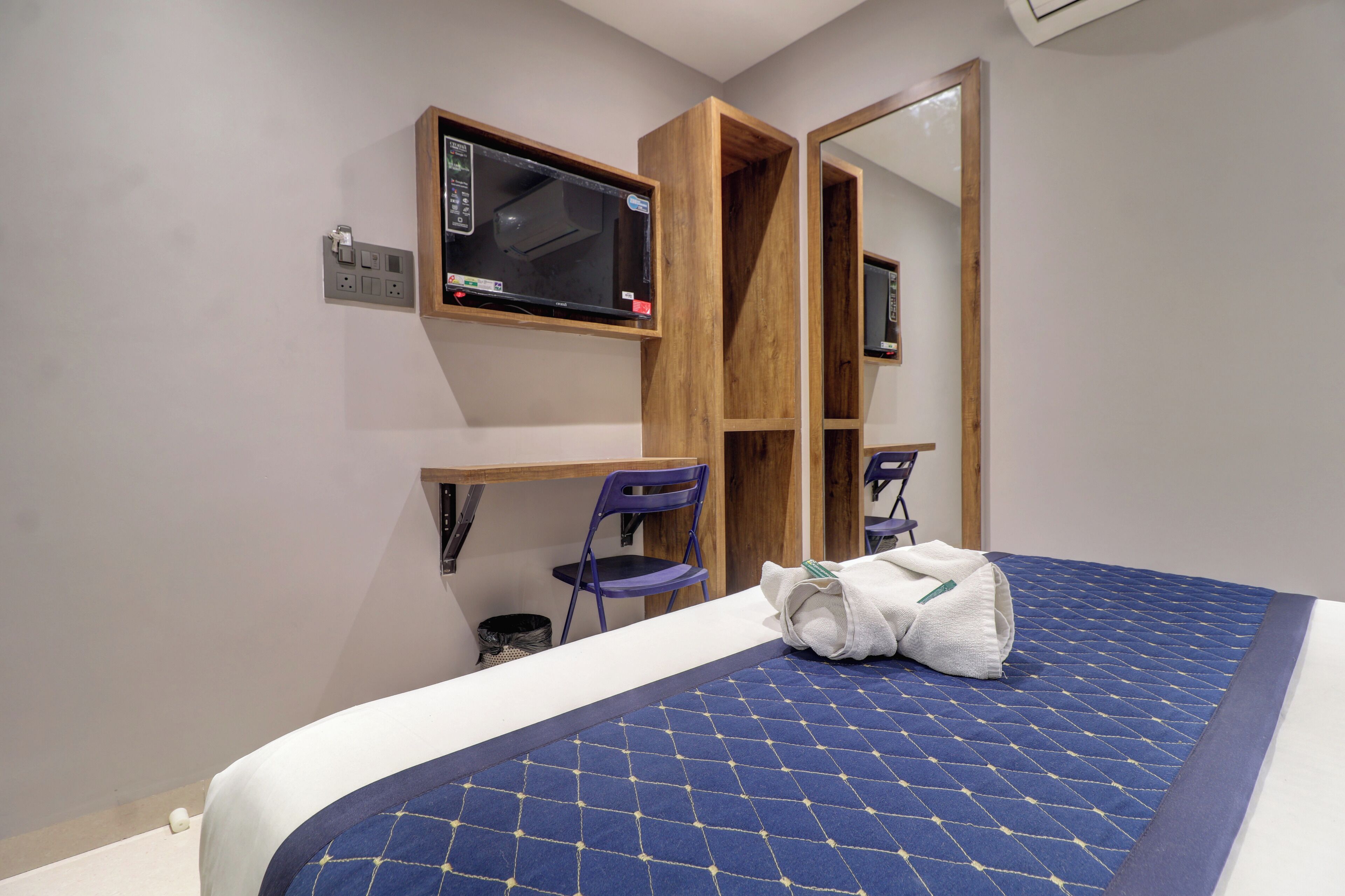 A bedroom with a bed, a desk, a chair, a mirror, and a microwave.