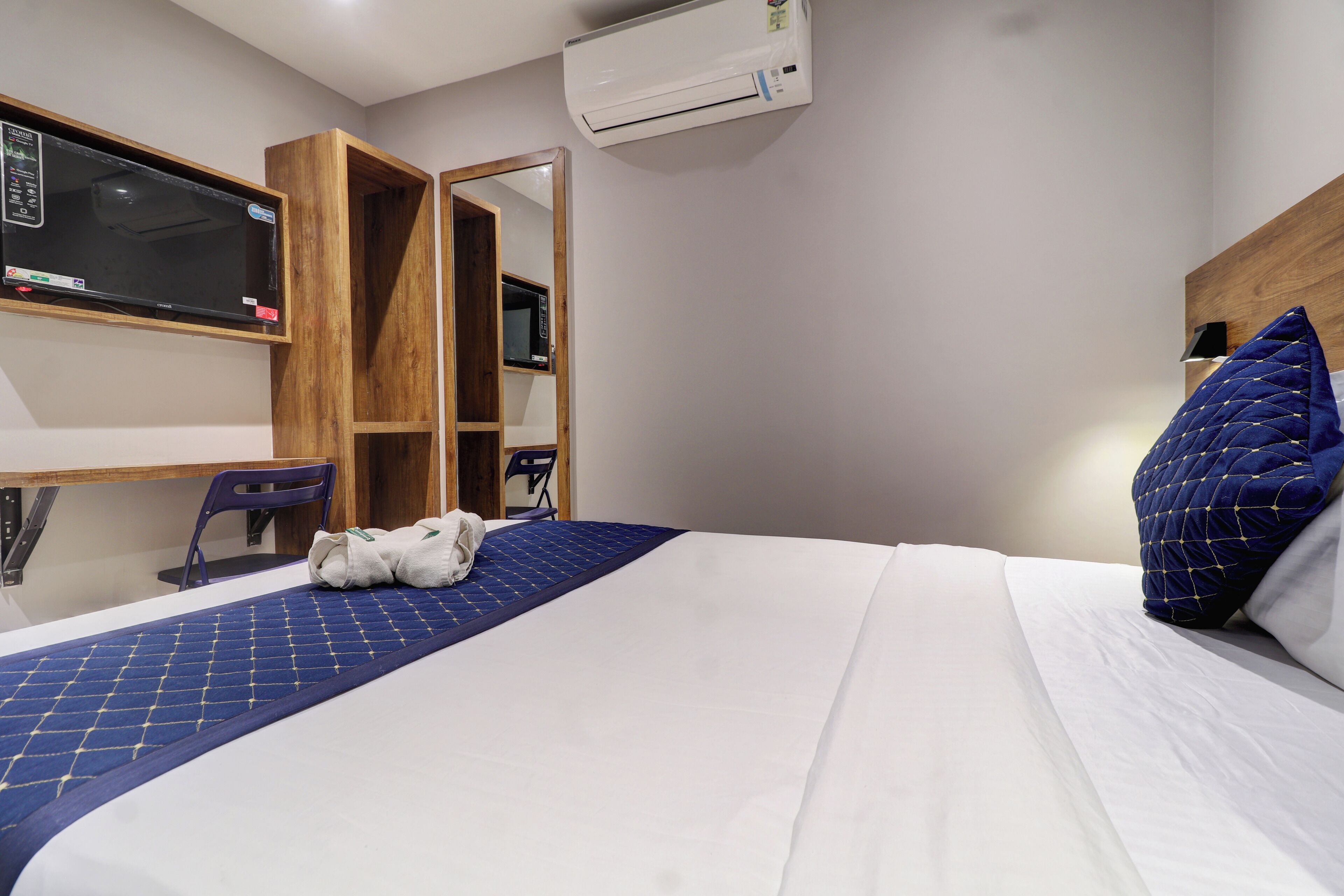 A hotel room with a bed, a desk, a chair, a wardrobe, and an air conditioning unit.