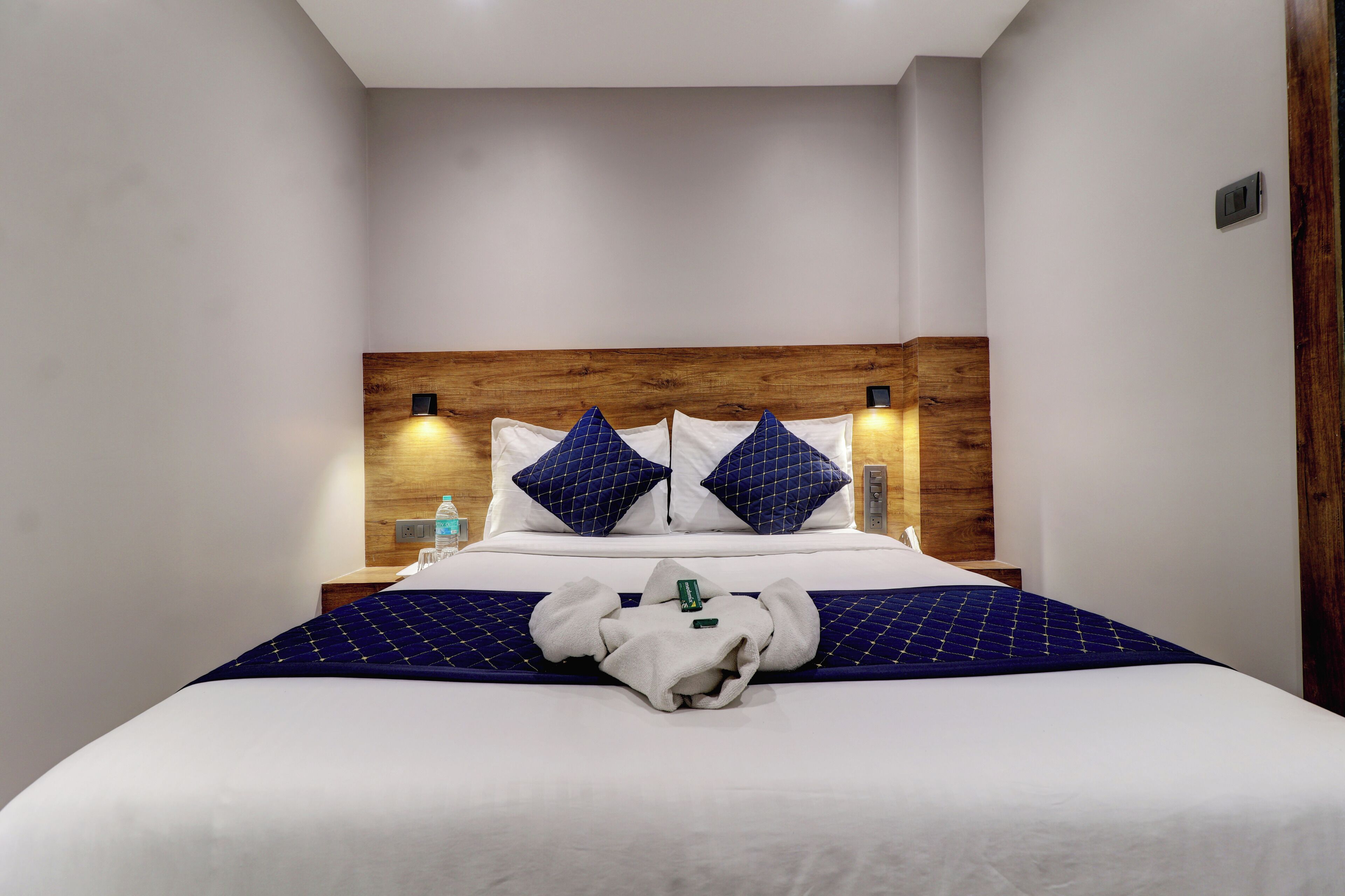 Una cama bien hecha con cabecera de madera, ropa de cama blanca y dos almohadas azules.