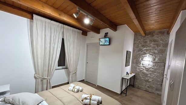 Ein Hotelzimmer mit Holzbalkendecke, einem Bett mit beigefarbener Bettwäsche, einem kleinen Tisch mit Fernseher und einer Steinwand.