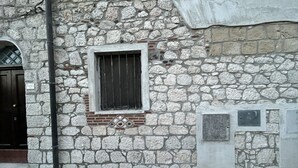 Ein Steinhaus mit einem Fenster mit Metallgitter, einer Tür und einer kleinen Plakette an der Wand.