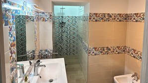 Ein Badezimmer mit einem weißen Waschbecken, einem Bidet und einer Dusche mit Mosaikfliesen.