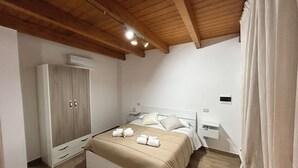 Ein Schlafzimmer mit Holzboden, einem Bett mit beigefarbener Bettwäsche, einem Kleiderschrank und einem Nachttisch.