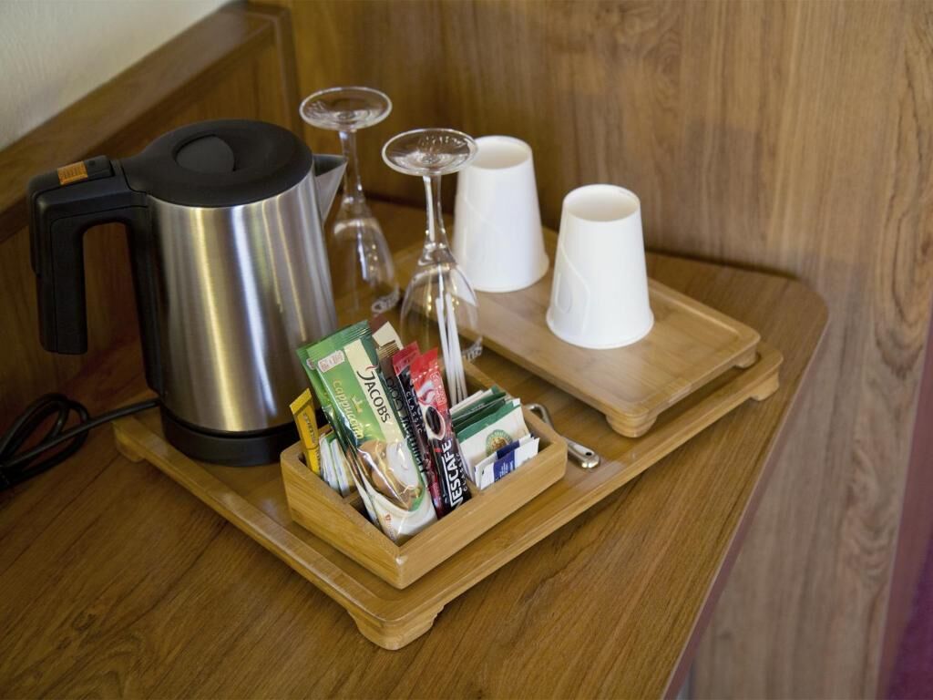 A wooden tray with a stainless steel kettle, a glass, and white cups on a wooden table.