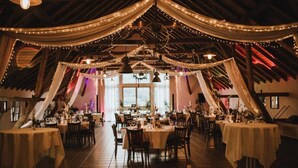 An indoor dining area with tables set for a meal, draped with white fabric and string lights. - Hotel Gutshof (Herborn)