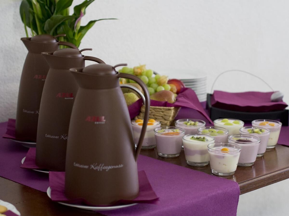 A table with a coffee pot, a basket of fruit, and several glasses of a purple beverage.