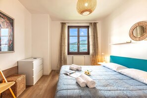 A bedroom with a bed, a window with a view, a dresser, and a wicker chair.