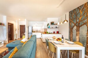 A modern kitchen with white cabinets, a dining area with a white table, and a living area with a blue sofa. - Casa Mia Menaggio (Menaggio)