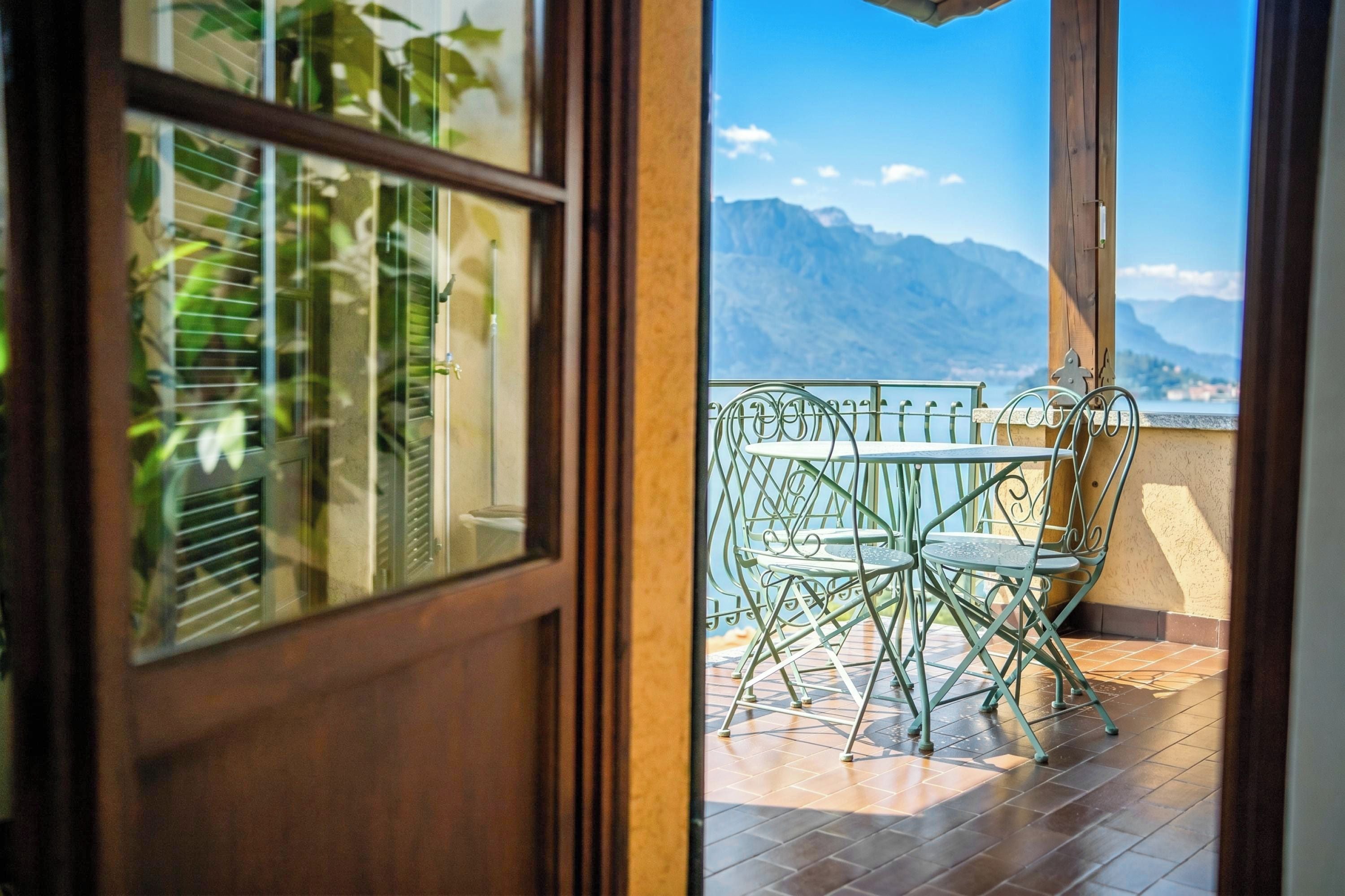 Een balkon met een tafel en stoelen, uitzicht op bergen en een houten deur.