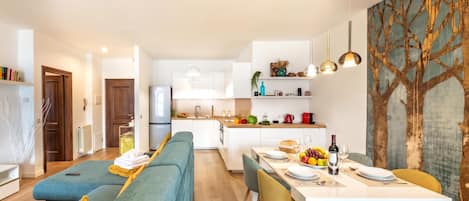 A modern kitchen with white cabinets, a dining area with a white table, and a living area with a blue sofa.
