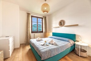 A bedroom with a bed, a window with curtains, a bedside table with a lamp, and a wall-mounted mirror. - Casa Mia Menaggio (Menaggio)