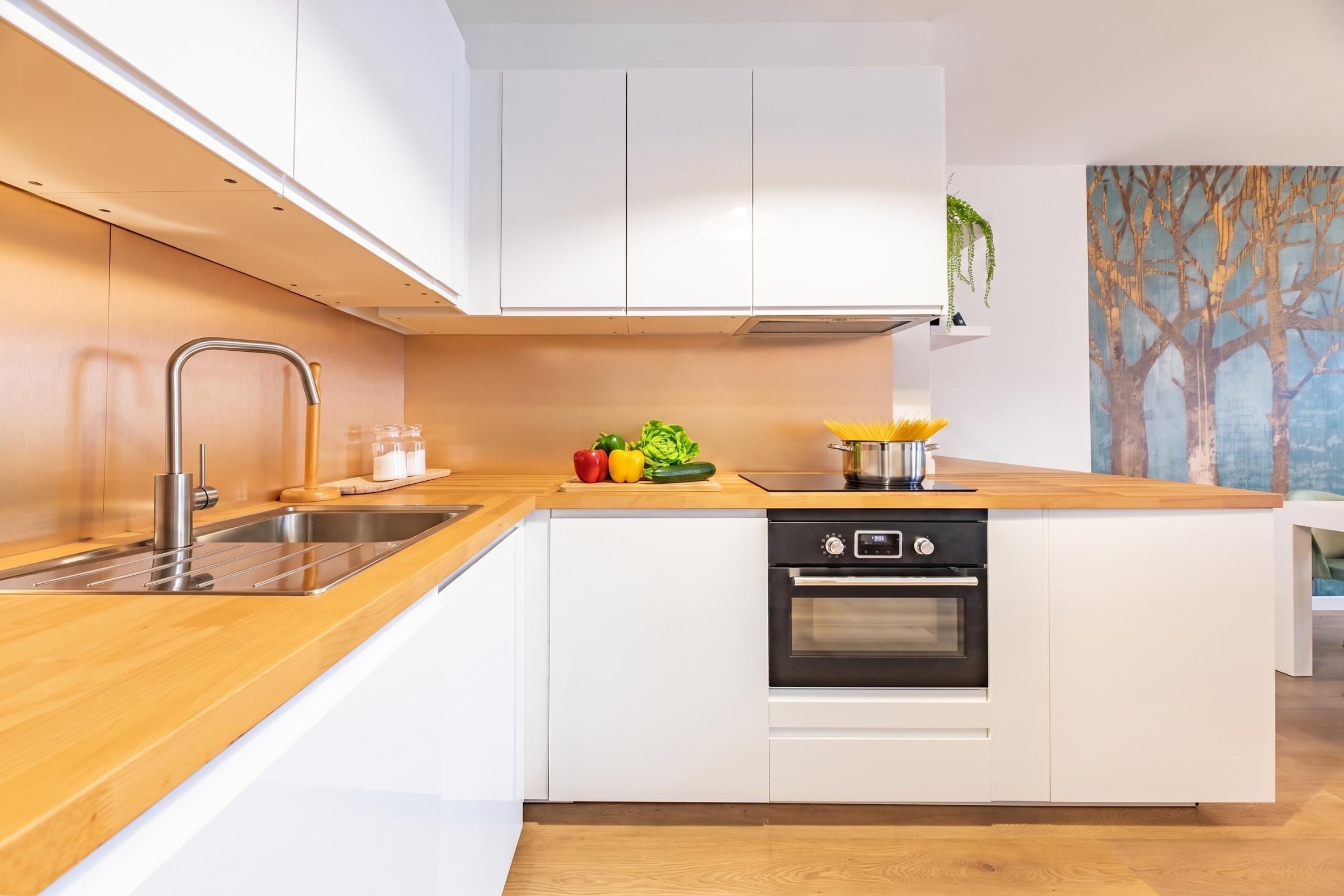 A modern kitchen with white cabinetry, a wooden countertop, a stainless steel sink, and an oven.