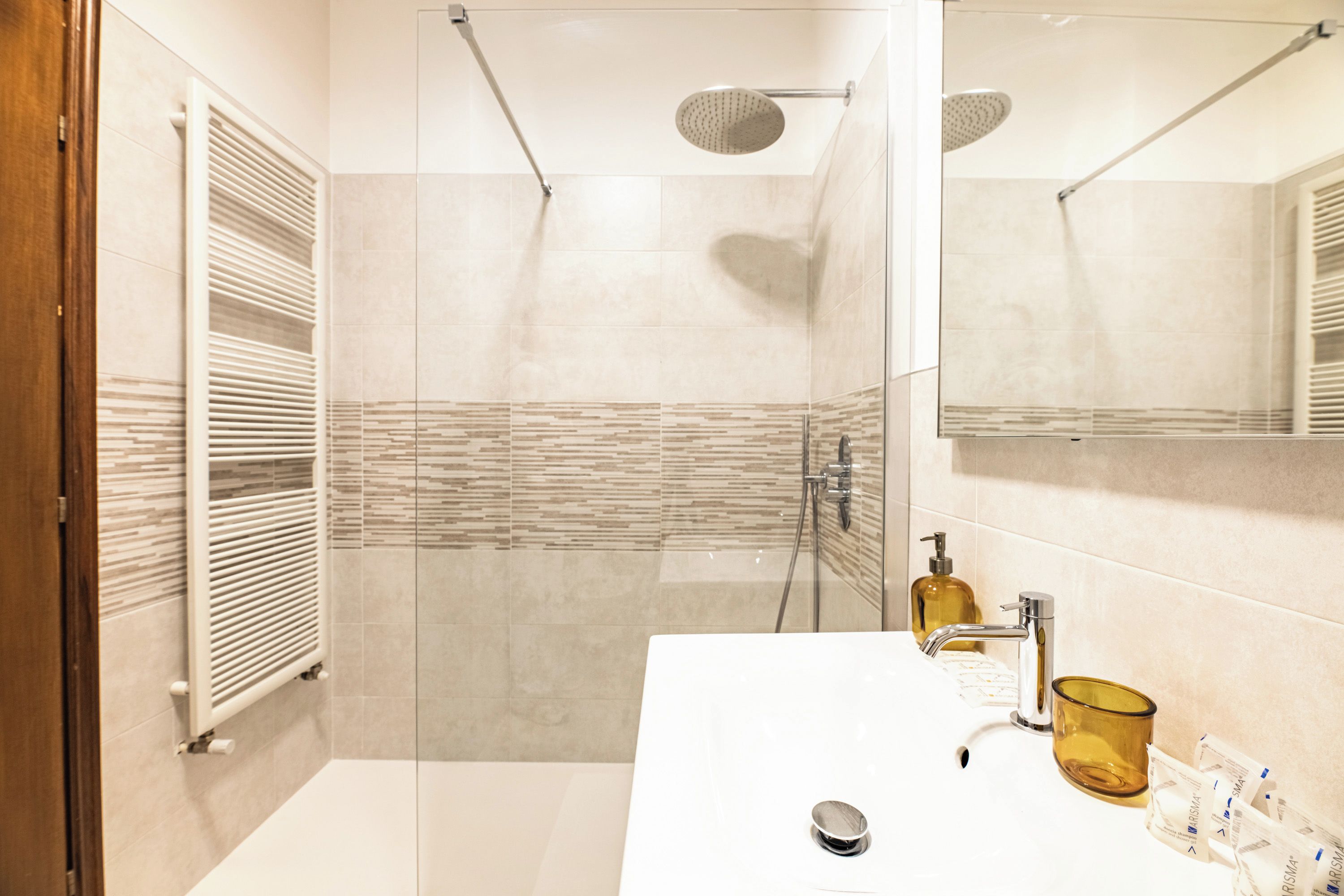 A modern bathroom with a glass-enclosed shower, a white sink with a mirror, and a towel rack.