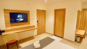 A hotel room with a bed, a desk, a chair, a television, and wooden doors. - Hotel Naveena Grand (Hyderabad)