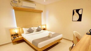 A hotel room with a large bed, bedside tables, a desk, and a chair. - Hotel Naveena Grand (Hyderabad)