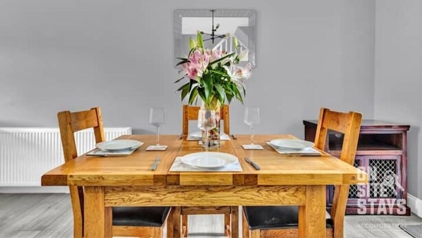 A dining area with a wooden table set for four, a vase with flowers, and a window with a view.