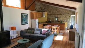 Un salon chaleureux avec un canapé, une petite table et une cheminée. Il y a également un coin cuisine avec des meubles en bois et un mur en pierre.