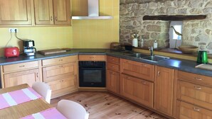 Une cuisine avec des meubles en bois, un mur en pierre, un pare-feu jaune et un lave-vaisselle Bosch.