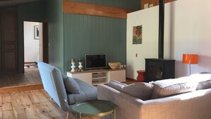 Un salon avec un fauteuil bleu, un canapé, une télévision et une cheminée.