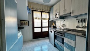 Cocina compacta con microondas, estufa y pileta. Se observa una ventana con cortinas y una puerta que da al exterior.